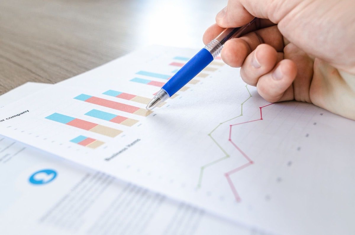 A hand with a pen reviewing printed spending charts and reports